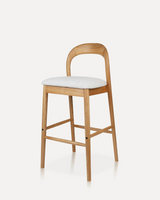 Modern solid wood bar stool with an arched backrest, upholstered fabric seat, and integrated footrest, available in rubberwood or ash wood for hotels, Airbnb properties, furnished apartments, cafés, and contemporary kitchens.